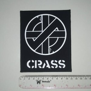 May include: Black and white embroidered patch with a circle containing a stylized anarchy symbol and the word "CRASS" below it.