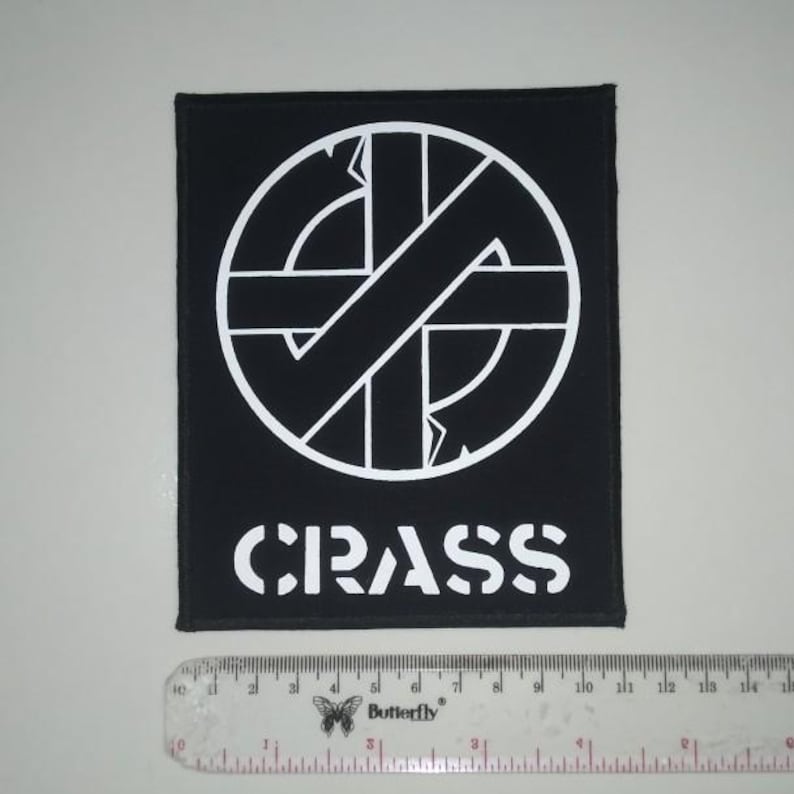 May include: Black and white embroidered patch with a circle containing a stylized anarchy symbol and the word "CRASS" below it.