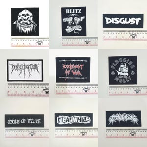 May include: A collection of nine rectangular fabric patches featuring various band logos and graphics in black and white. Each patch is displayed next to a ruler showing measurements in centimeters, with designs including skulls, ships, and stylized text.
