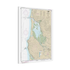 May include: A framed nautical chart of Tillamook Bay, Oregon. The chart features detailed information, including depth soundings, navigational aids, and coastline details. The color palette includes shades of blue, green, and tan, with a white frame.