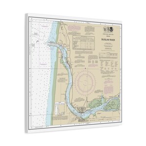 May include: A framed nautical chart of the Siuslaw River, Oregon, with a white border. The chart features detailed information, including depth soundings, navigational aids, and the river's course. The chart is in shades of blue, green, and beige.