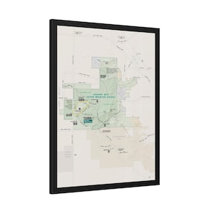 May include: A framed map print of the Saguaro West Tucson Mountain District, featuring a light beige background with green shaded park areas, black road lines, and text labels for trails, visitor centres, and scenic loops in a black frame.