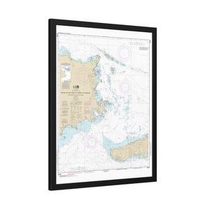 May include: Framed nautical chart of a coastal area, featuring detailed lines, symbols, and text. The chart has a beige and blue color scheme, with a black frame. The chart appears to be a map of a coastal region.