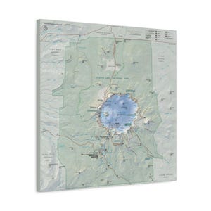 May include: A square wall art print featuring a detailed topographic map of Crater Lake National Park. The map displays the central blue lake, surrounding mountain terrain in muted green and gray tones, park boundaries, roads, and trail markers.