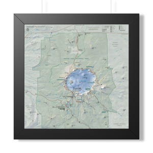 May include: A framed topographic map of Crater Lake National Park featuring a central blue lake surrounded by green terrain, marked trails, and park infrastructure. The map is enclosed in a simple black frame with a clean, professional aesthetic.