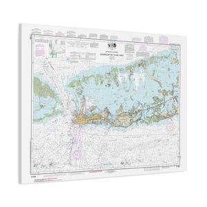 May include: A nautical chart of Sugarloaf Key to Key West, Florida, featuring detailed coastlines, water depths, and navigational markers. The map uses a color palette of blue, green, and beige, with text labels and symbols. The chart is mounted on a white background.