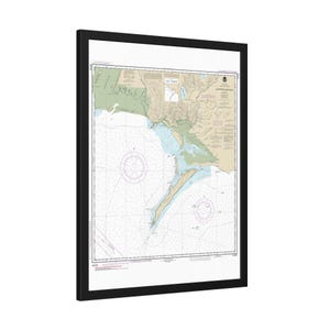 May include: A framed nautical chart of the Outer Banks, North Carolina, showing coastlines, depths, and navigational aids. The chart is in blue, green, and tan, with a black frame and white mount.