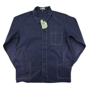 May include: A navy blue work jacket with white stitching. It has a collared neckline, a chest pocket, and two lower pockets. A tag with text hangs from the collar. The jacket has long sleeves and a button-up front.