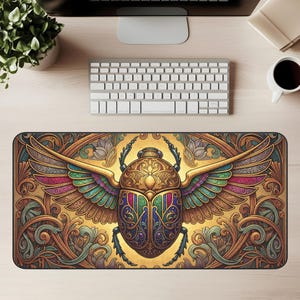 Puede incluir: Alfombrilla de escritorio rectangular con una ilustración detallada de un escarabajo dorado con alas coloridas. Las alas muestran tonos de rosa, verde y azul. El fondo es una mezcla de oro y marrón con adornos ornamentados.