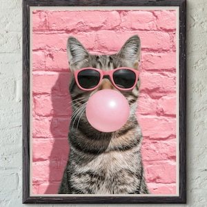 May include: Framed print featuring a tabby cat wearing pink sunglasses and blowing a large pink bubblegum bubble. The cat is set against a pink brick wall background. The frame is black.