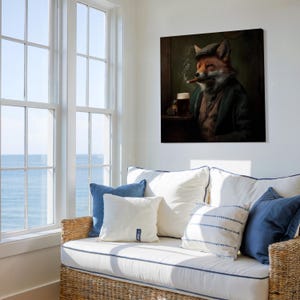 May include: A framed canvas art print depicts a fox in a tweed cap and jacket, smoking a cigar and holding a beer. The artwork has a vintage aesthetic, with a dark, moody color palette. The print is displayed above a white couch with blue pillows.