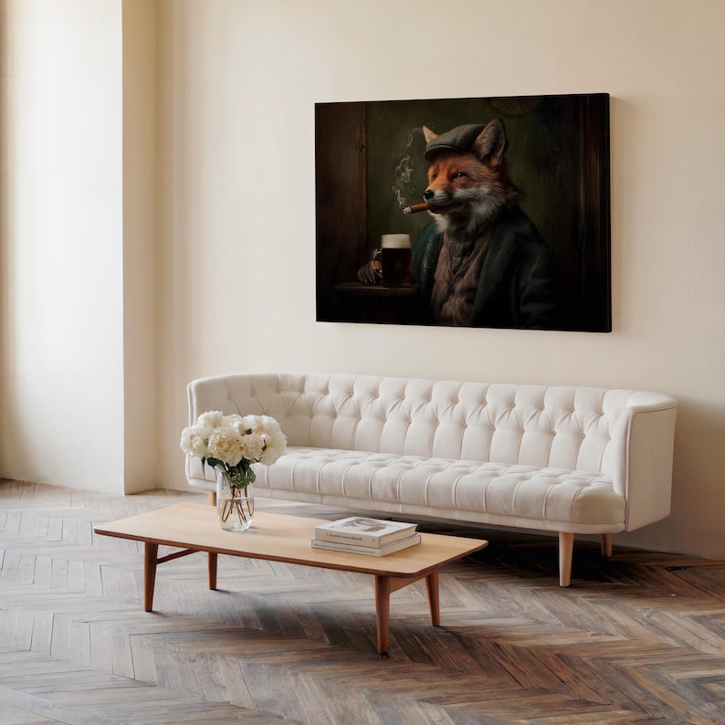 May include: A framed canvas art print depicts a fox in a tweed cap and jacket, smoking a cigar and holding a beer. The artwork hangs above a white tufted sofa and a wooden coffee table with books and a vase of flowers.
