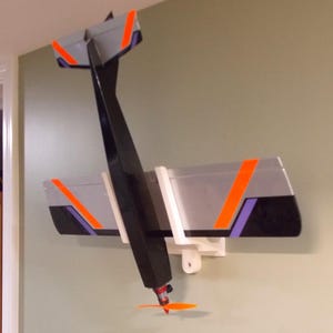 May include: A white wall mount with a black and silver airplane model attached. The airplane has orange accents and a propeller.