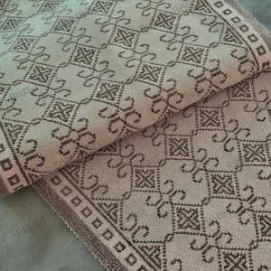 Könnte beinhalten: Beige und braun gemusterter Teppich mit geometrischem Design. Der Teppich weist ein sich wiederholendes Muster aus Quadraten und scrollartigen Formen auf. Die Kanten sind mit einem braunen Rand versehen.