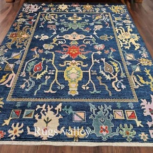 Könnte beinhalten: Ein rechteckiger, marineblauer Teppich mit einem aufwendigen, farbenfrohen Blumenmuster. Der Teppich hat ein zentrales Design mit roten, gelben und grünen Elementen, umgeben von einem Rand mit ähnlichen Farben. Der Text "Rugs Valley" ist sichtbar.