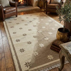 Könnte beinhalten: Ein rechteckiger Teppich mit zweifarbigem Design, bestehend aus einem hellbeigen und einem dunkelbraunen Bereich. Der Teppich ist mit einem wiederkehrenden Muster aus kleinen weißen und braunen sternförmigen Motiven verziert und hat Fransen.