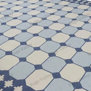 May include: A geometric patterned rug featuring a repeating design of octagons in light blue, off-white, and navy blue. The rug's border has a decorative pattern. The overall design is symmetrical and visually appealing, suitable for various interior settings.