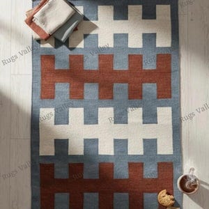 Könnte beinhalten: Ein Set aus drei Keramikbechern mit gesprenkelter, cremefarbener Glasur. Jeder Becher zeigt ein handgemaltes Design: ein blau-grünes Blatt, eine gelbe Blume und eine rote Beere. Die Becher haben eine einfache, abgerundete Form.