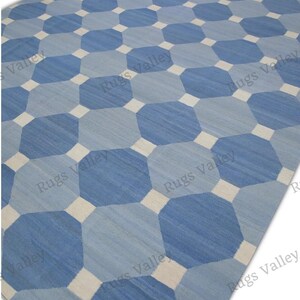 Könnte beinhalten: Ein großer Teppich mit geometrischem Muster. Er zeigt ein sich wiederholendes Muster aus blauen Achtecken in verschiedenen Schattierungen, unterbrochen von weißen Quadraten. Die Farbgebung ist blau und weiß und sorgt für einen modernen und stilvollen Look.