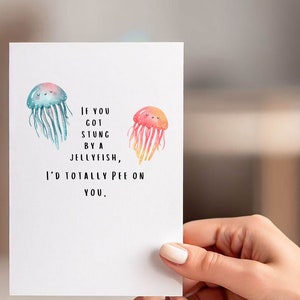 May include: A white card with a humorous message about jellyfish. The card features two cartoon jellyfish with smiling faces. The text reads: "If you got stung by a jellyfish, I'd totally pee on you."