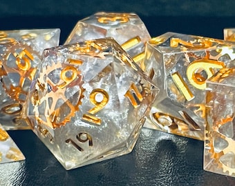 May include: A set of clear, iridescent dice with gold gears and numbers. The dice are made of resin and have a steampunk aesthetic.