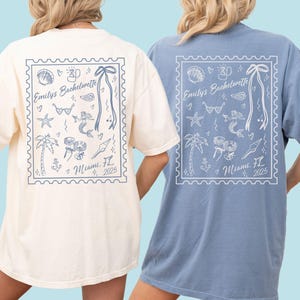 Peut inclure: T-shirts ivoire et bleu jean avec un motif en forme de timbre-poste au dos. Le motif comprend le texte "Emily's Bachelorette" et "Miami, FL 2025", ainsi que des illustrations de coquillage, lunettes de soleil, sirène et palmier.
