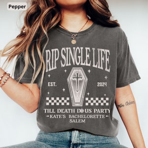 May include: A pepper-coloured t-shirt featuring the text "RIP SINGLE LIFE" above a coffin graphic and the text "EST. 2024". Below the coffin is "TILL DEATH DOUS PARTY - KATE'S BACHELORETTE - SALEM". The shirt has a vintage, distressed appearance.