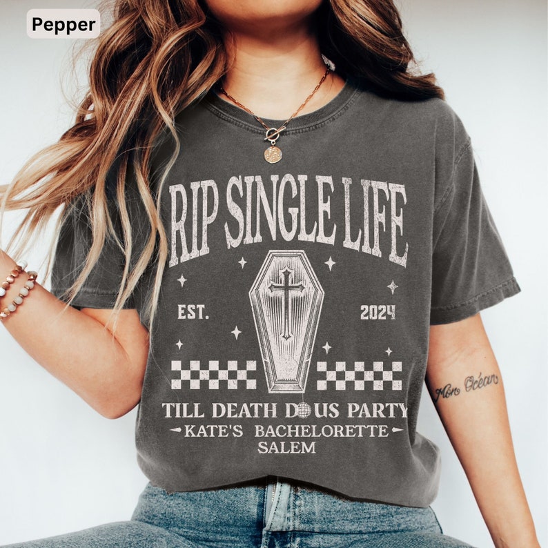 May include: A pepper-coloured t-shirt featuring the text "RIP SINGLE LIFE" above a coffin graphic and the text "EST. 2024". Below the coffin is "TILL DEATH DOUS PARTY - KATE'S BACHELORETTE - SALEM". The shirt has a vintage, distressed appearance.
