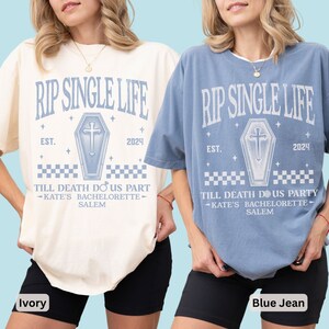 May include: Two short-sleeved t-shirts, one ivory and one blue jean, with the text "RIP SINGLE LIFE" above a coffin graphic. Below the graphic are the words "TILL DEATH DO US PART - KATE'S BACHELORETTE - SALEM". The shirts are part of a bachelorette party theme.