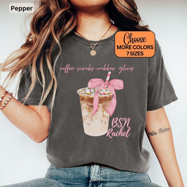 May include: Pepper-colored t-shirt featuring a watercolor illustration of an iced coffee drink with a pink bow and straw. The text includes "coffee scrubs rubber gloves" and "BSN Rachel". The shirt also has a box that says "Choose More Colors 7 Sizes".