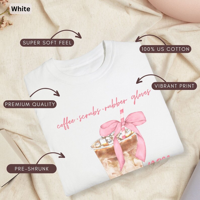 May include: White t-shirt with a watercolor illustration of an iced coffee drink with a pink bow and straw. The text "coffee scrubs rubber gloves" is written in pink script. Features include 100% US cotton, pre-shrunk, premium quality, and a super soft feel.