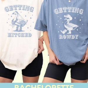 Puede incluir: Dos camisetas de gran tama&ntilde;o, una crema y otra azul, con gr&aacute;ficos a juego. La camiseta crema dice "Getting Hitched" con una ilustraci&oacute;n de ganso. La camiseta azul dice "Getting Rowdy" con un ganso con sombrero de vaquero. Pantalones cortos de ciclista negros.