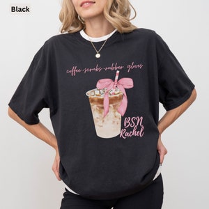 May include: Black t-shirt with a watercolor illustration of an iced coffee drink with a pink bow and straw. The shirt has the text "coffee scrubs rubber gloves" and "BSN Rachel" in pink script.