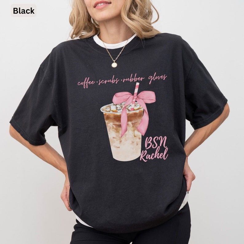 May include: Black t-shirt with a watercolor illustration of an iced coffee drink with a pink bow and straw. The shirt has the text "coffee scrubs rubber gloves" and "BSN Rachel" in pink script.