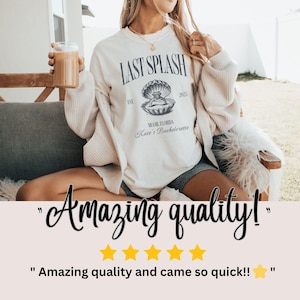 May include: Cream-colored sweatshirt with the text "LAST SPLASH" and a seashell graphic. The graphic includes the text "MIAMI FLORIDA Kate's Bachelorette" and the year "2025". The sweatshirt is worn by a person.