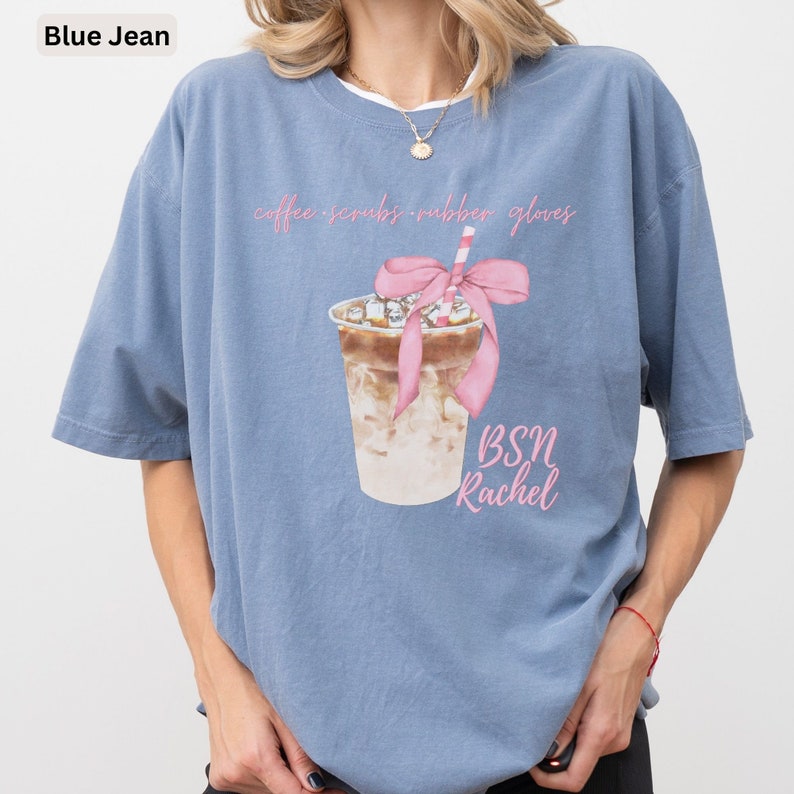 May include: Blue jean colored t-shirt with a graphic of an iced coffee drink with a pink bow and straw. The text on the shirt says "coffee scrubs rubber gloves" and "BSN Rachel".