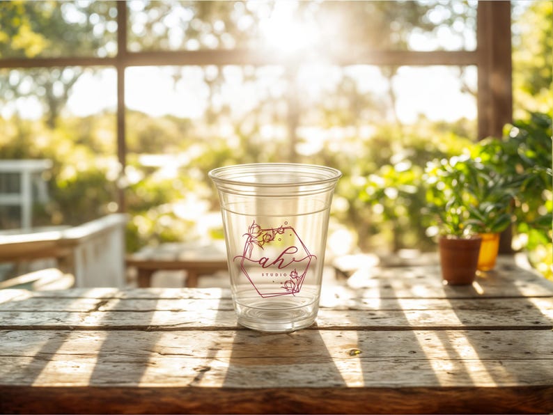 May include: A clear plastic cup with a pink and yellow floral design and the text "Lah Studio" on a wooden table.