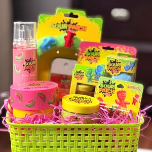 May include: A green woven basket filled with Sour Patch Kids-themed products. Includes a pink body butter container with watermelon slices, a pink spray bottle, and various boxes and jars with the Sour Patch Kids logo. Pink shredded paper fills the basket.
