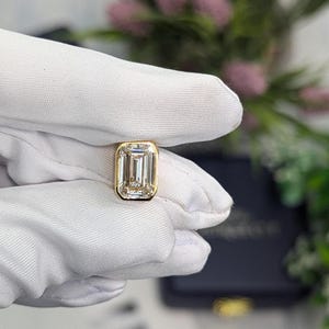 K&ouml;nnte beinhalten: Ein goldener Ring mit einem gro&szlig;en, klaren Smaragdschliff-Diamanten.