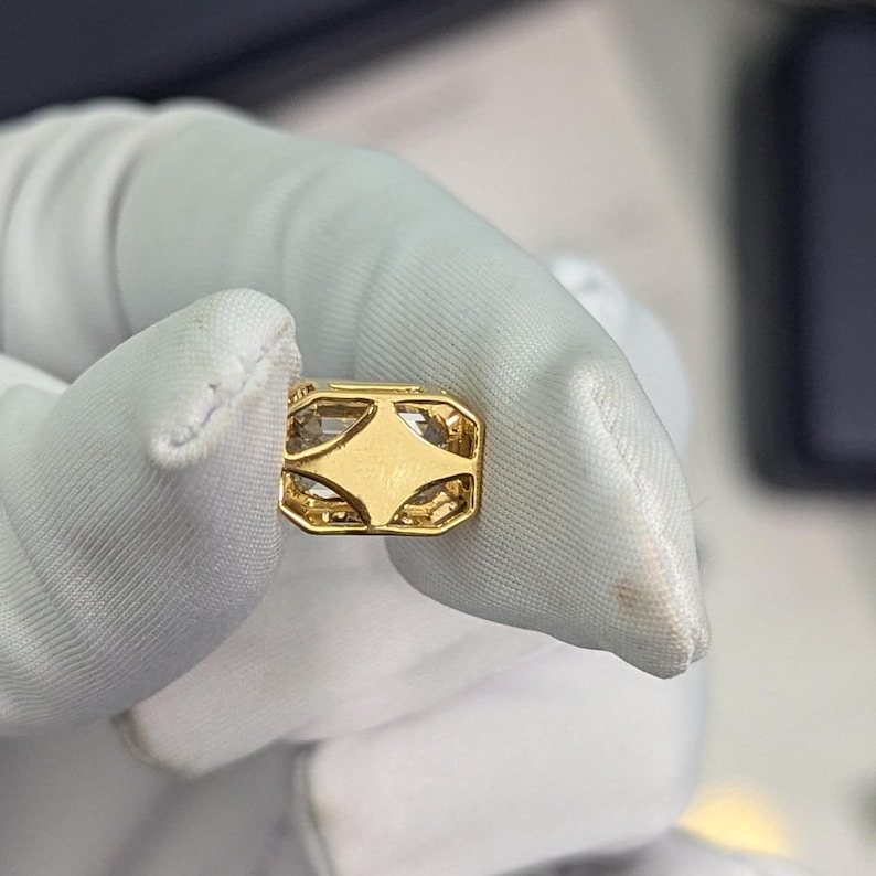 K&ouml;nnte beinhalten: Ein goldener Anh&auml;nger mit einem klaren Stein, der in einem geometrischen Design gefasst ist.