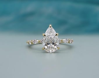 May include: A gold ring featuring a large pear-shaped center diamond held by six prongs. The band is crafted from yellow gold and is accented with smaller marquise-cut diamonds set along the sides of the ring shank.