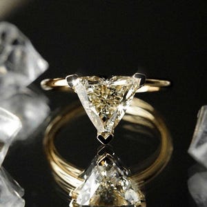 May include: A gold ring with a triangular diamond set in the center. The diamond is clear and has a slight yellow hue.