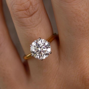 May include: A gold engagement ring with a large, round, clear diamond.