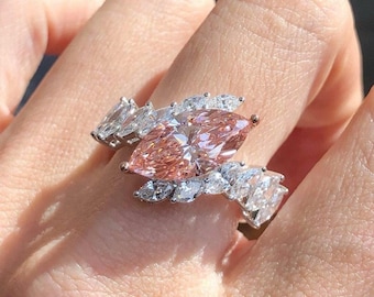 May include: A close-up of a ring featuring a large, pink marquise-cut gemstone as the focal point. The ring is adorned with smaller, clear gemstones, creating a sparkling, elegant design. The ring is set on a silver band.