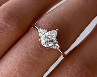 May include: A pear-shaped diamond engagement ring with a halo of smaller diamonds set in a gold band.