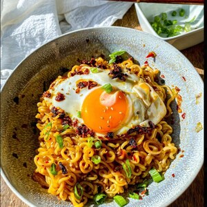 May include: A bowl of ramen noodles topped with a fried egg, green onions, and chili flakes.