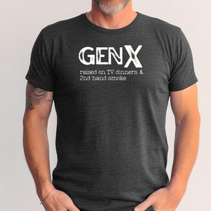 May include: A dark gray t-shirt with the text "GENX" in white, and the phrase "raised on TV dinners & 2nd hand smoke" in white below it.