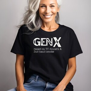 May include: A black t-shirt with white text that reads "GENX raised on TV dinners & 2nd hand smoke". A woman is wearing the shirt and smiling at the camera.