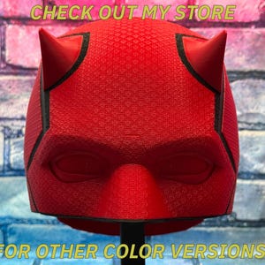 May include: A red mask with two horns, resembling a superhero's headgear. The mask has a textured surface and black trim. The text "CHECK OUT MY STORE" and "FOR OTHER COLOR VERSIONS!" are displayed in yellow.