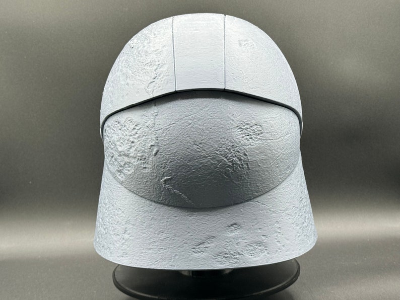 May include: A white helmet with a textured surface. The helmet has a raised ridge on the top and a visor.